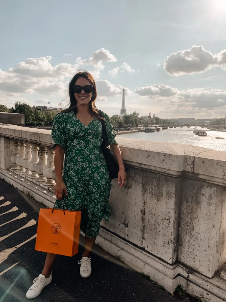 Woman wearing green dress with white and holding orange bag.