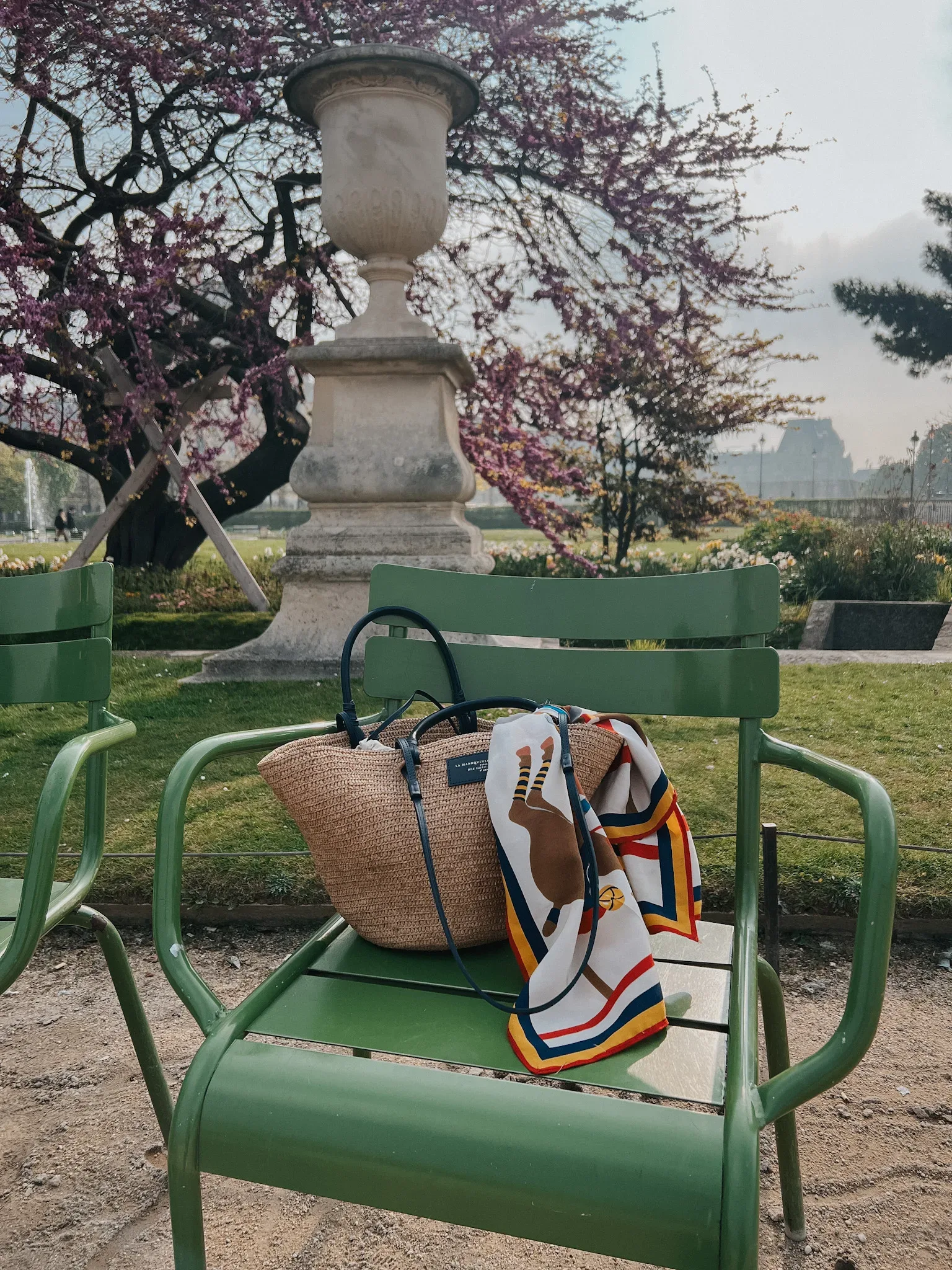 Basket bag sitting on a green chair with a scarf in the Tuileries.