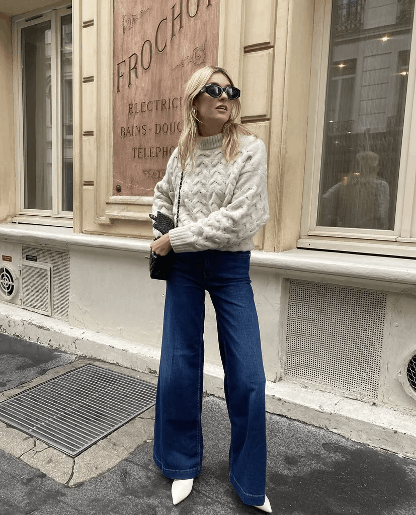 blonde girl standing with cream sweater and dark denim