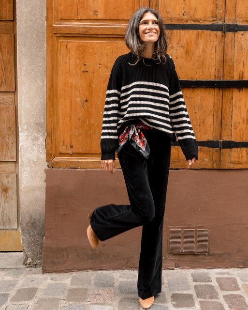 Black and white stripe sweater, black pants, brown boots, and scarf around waist is what a lady is wearing against a brown door