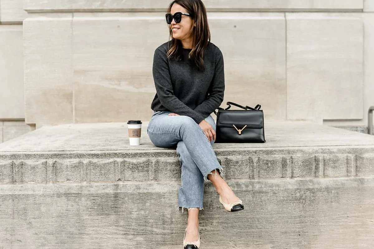 Sitting wearing dark grey cashmere sweater with sunglasses, blue denim, and flats