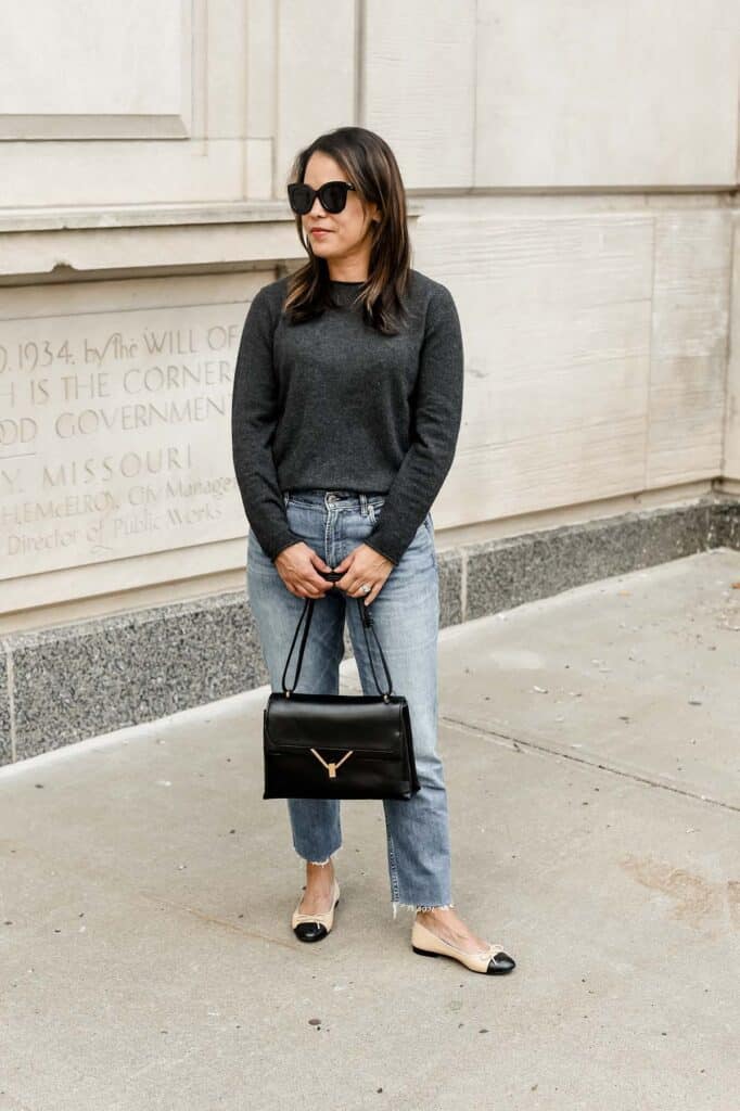 standing with black handbag and wearing a dark grey sweater