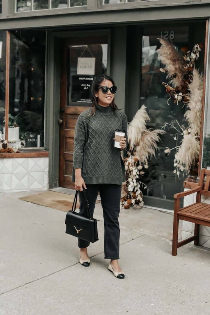 Standing holding coffee cup with green sweater and sunglasses on