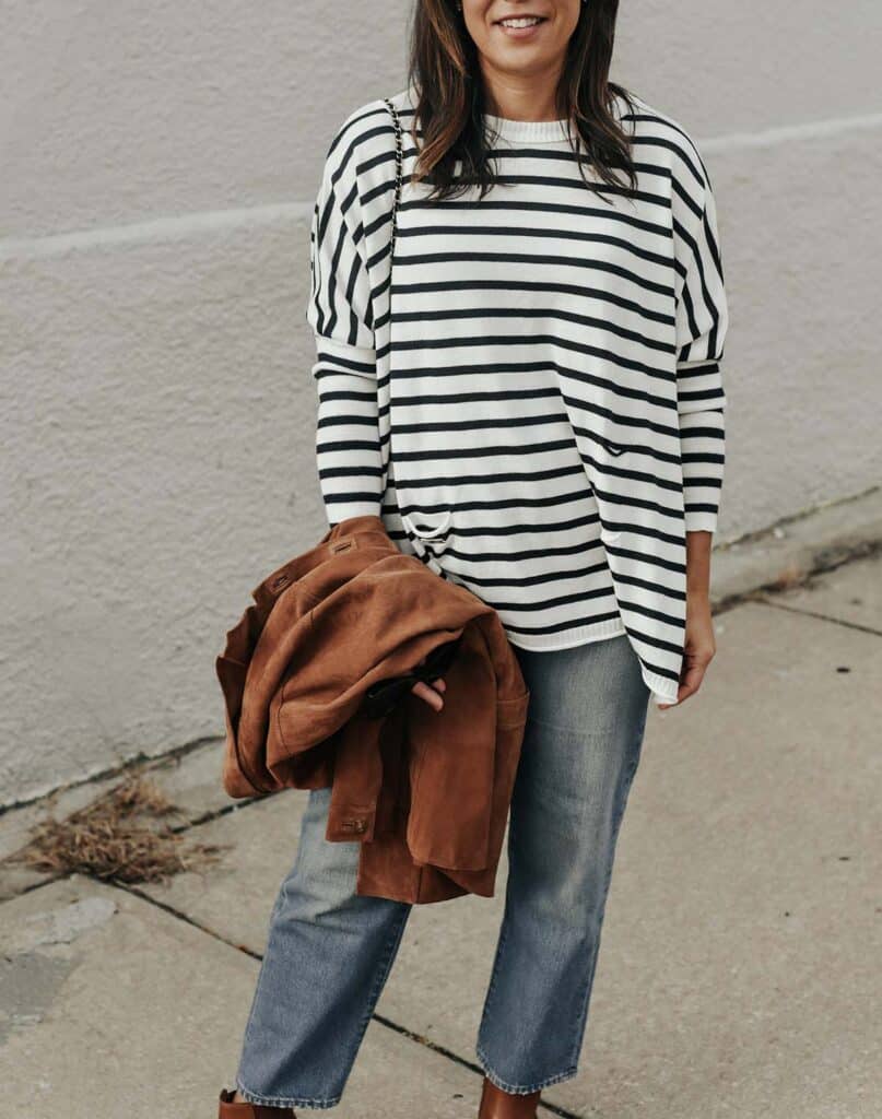 wearing a navy and white striped top on a street holding a suede brown jacket