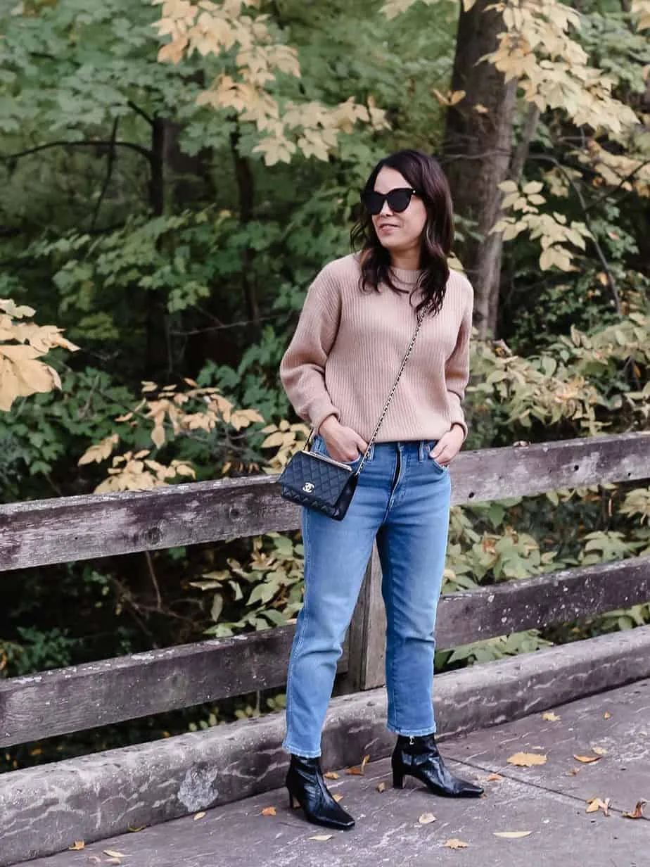 brown sweater, jeans, booties, in front of fall looking trees