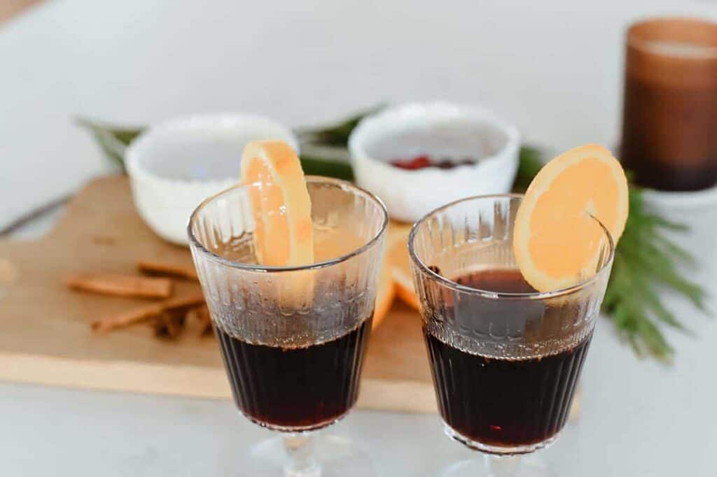 Two glasses of French vin chaud with orange slices sitting on a counter.