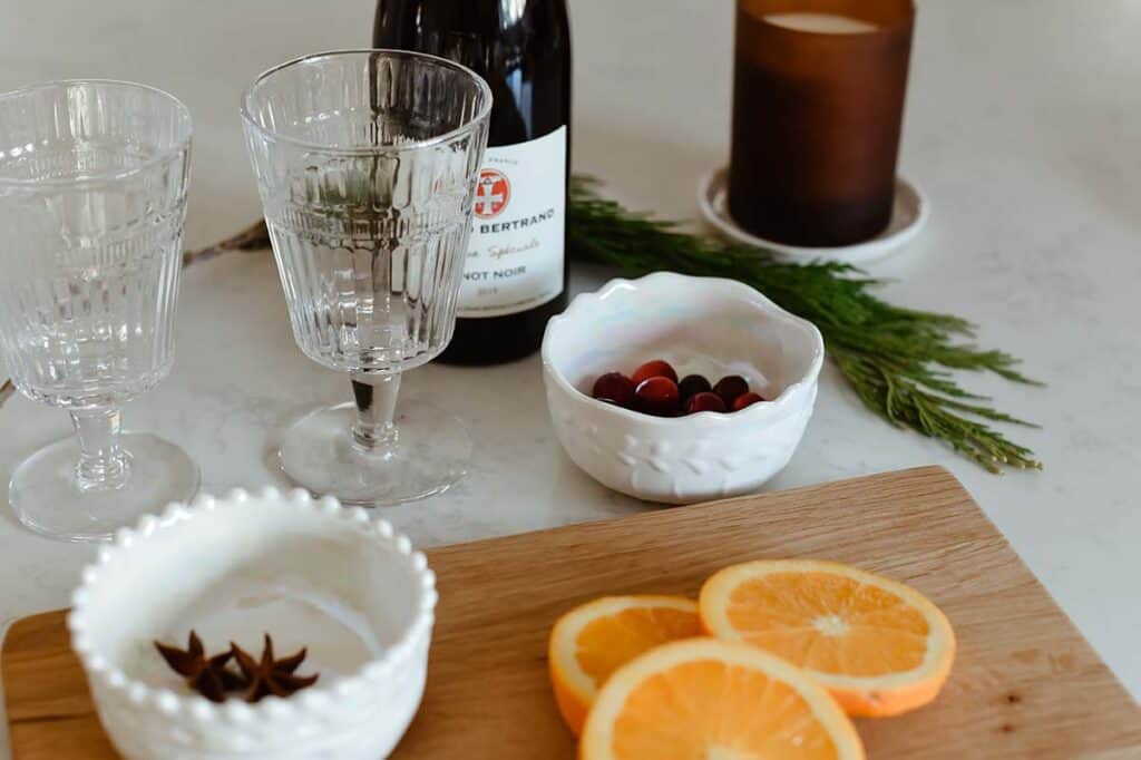 French Vin Chaud ingredients oranges, wine glass, candle, wine bottle sitting on counter