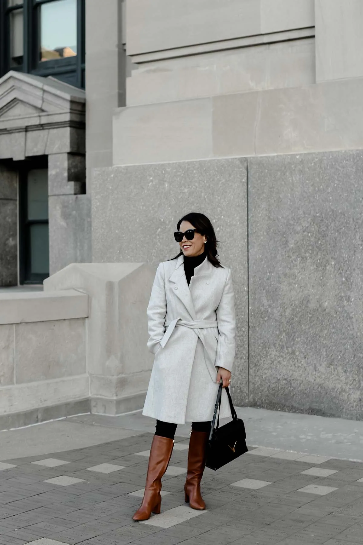 Standing in front of a building with grey coat and black bag