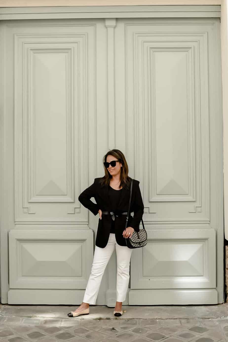 standing against door wearing black blazer and white denim