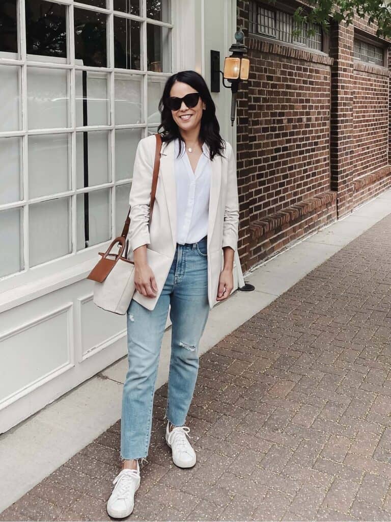 wearing jeans with white blazer and top standing outside a window