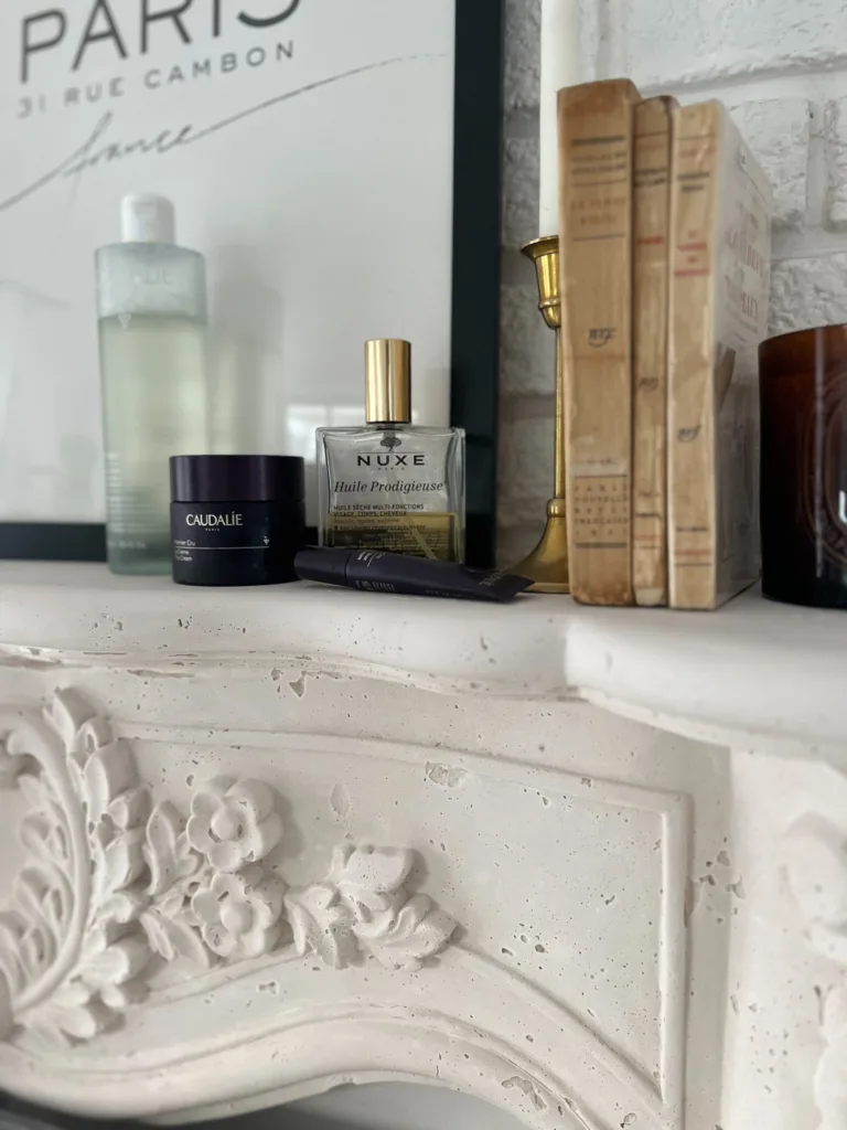 Beauty products sitting on a fireplace mantle which are part of living a french lifestyle. Caudalie toner, face cream, and eye cream plus body oil.