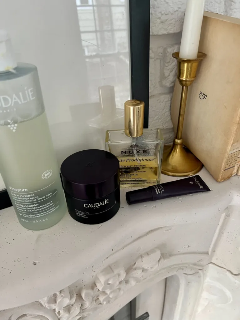 Beauty products sitting on a fireplace mantle which are part of living a french lifestyle. Caudalie toner, face cream, and eye cream plus body oil.