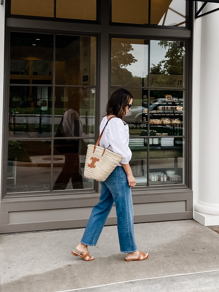 wearing jeans walking in white tee and straw tote