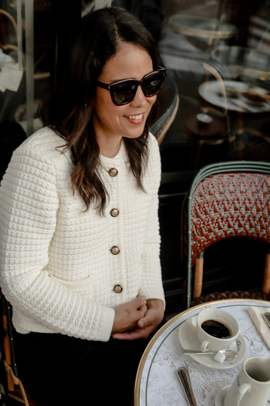 Sitting at Cafe in Paris wearing Ivory Bash Paris Sweater