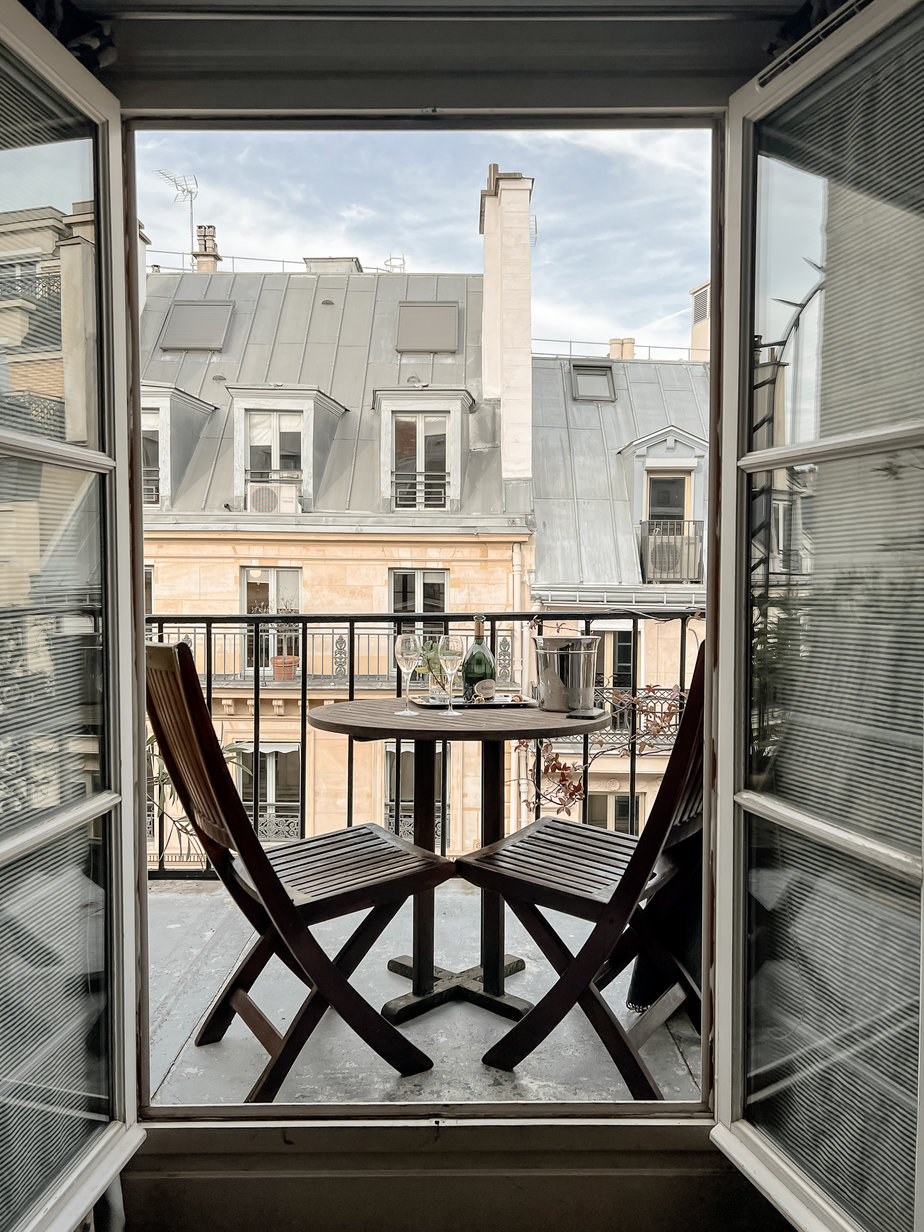 doors open and two chairs and a table with paris in the back
