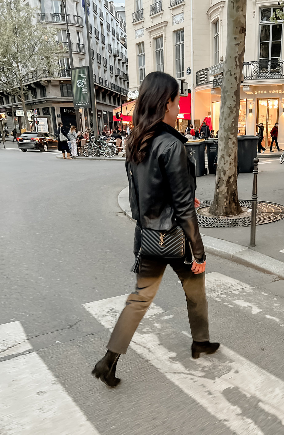 wearing black leather jacket, jeans, and black booties walking down street for what to pack for paris in fall.
