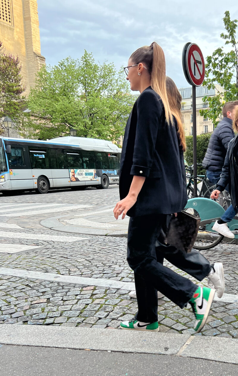 girl with navy blazer, black jeans, and nikes walking down street in paris