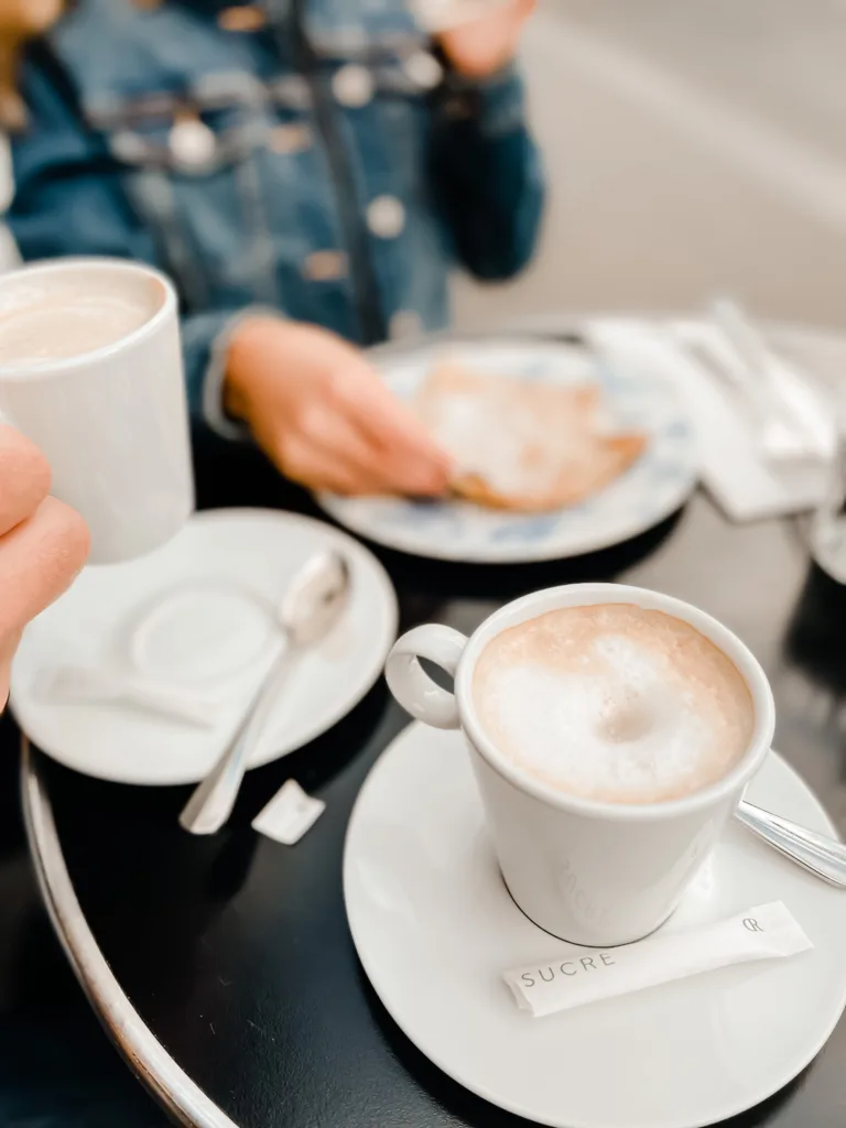 Coffee cup with foam sitting on a table with sucre packet. A way to order coffee in Paris.