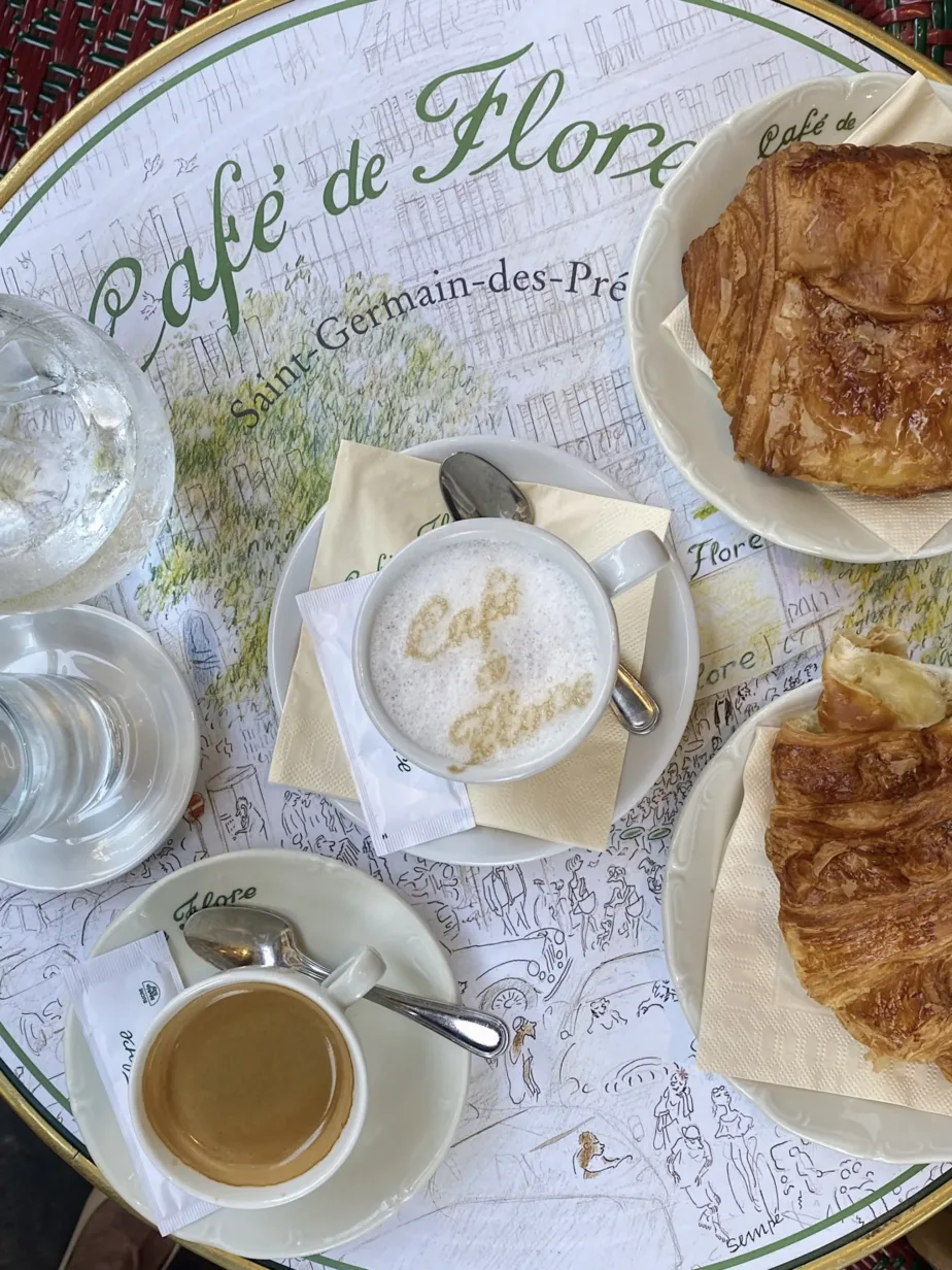 Latte with cafe de flore written on it sitting on a table with croissants and water in Paris.