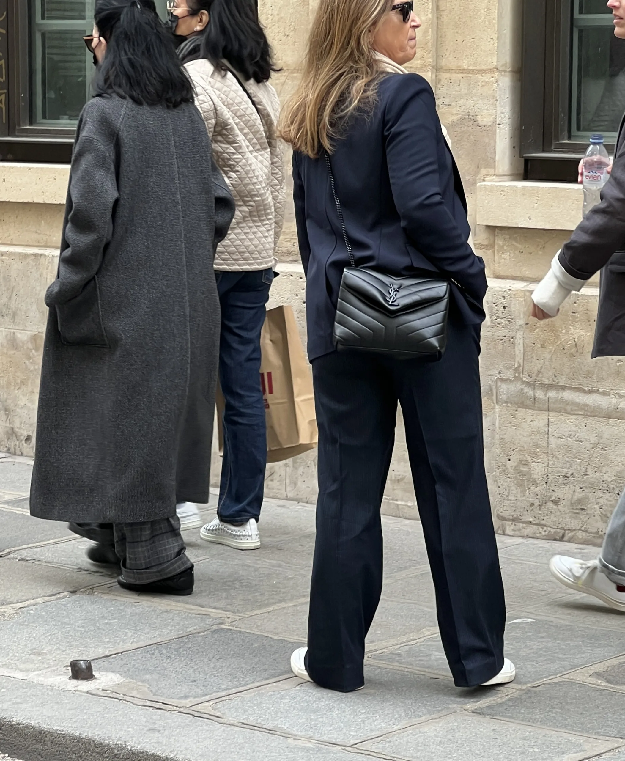 Woman walking wearing dark navy suit with YSL bag, everyday Parisian street style.
