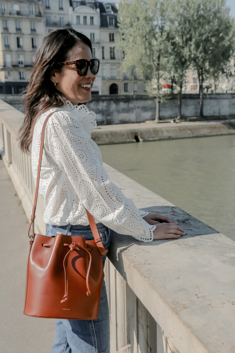 standing in white blouse white bag on bridge in paris