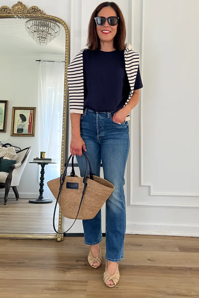 Lady wearing jeans, gold sandals, navy top, and stripe sweater.