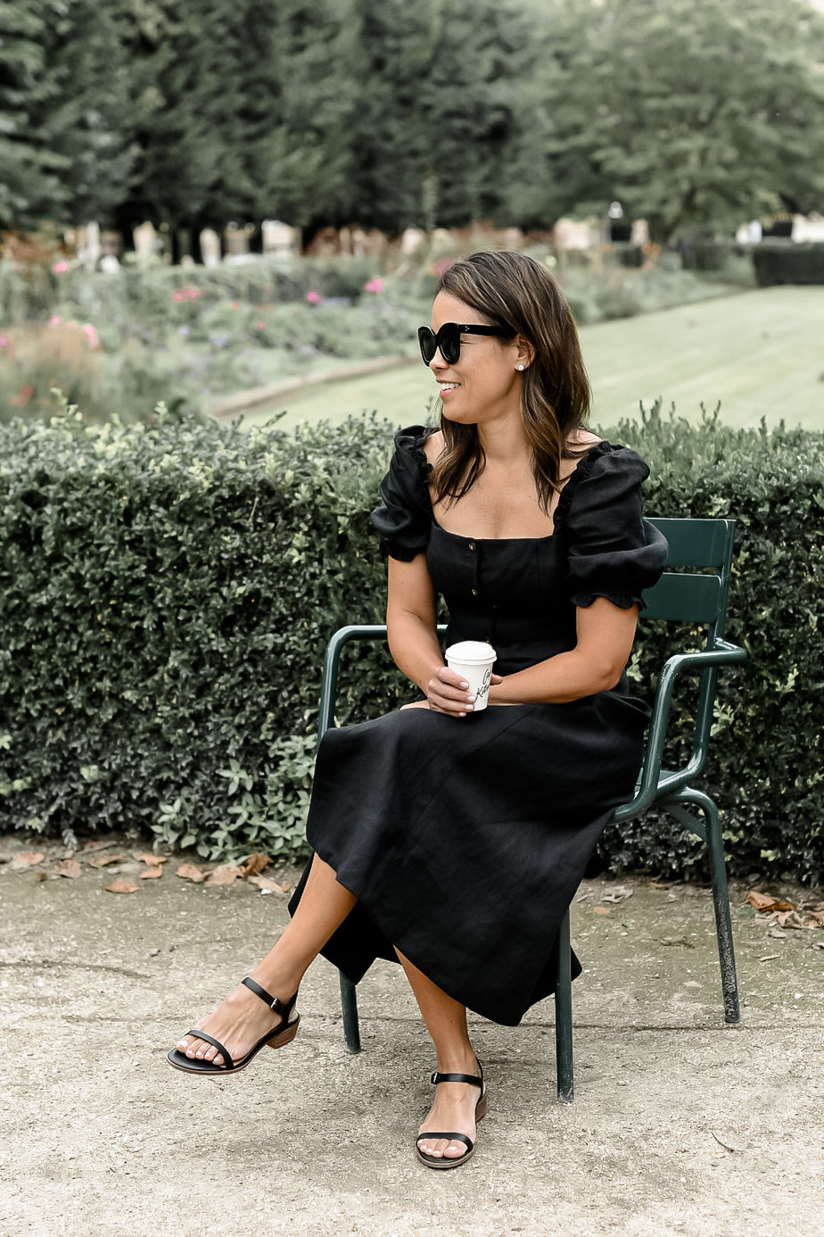 sitting in garden with black dress and holding coffee cup 