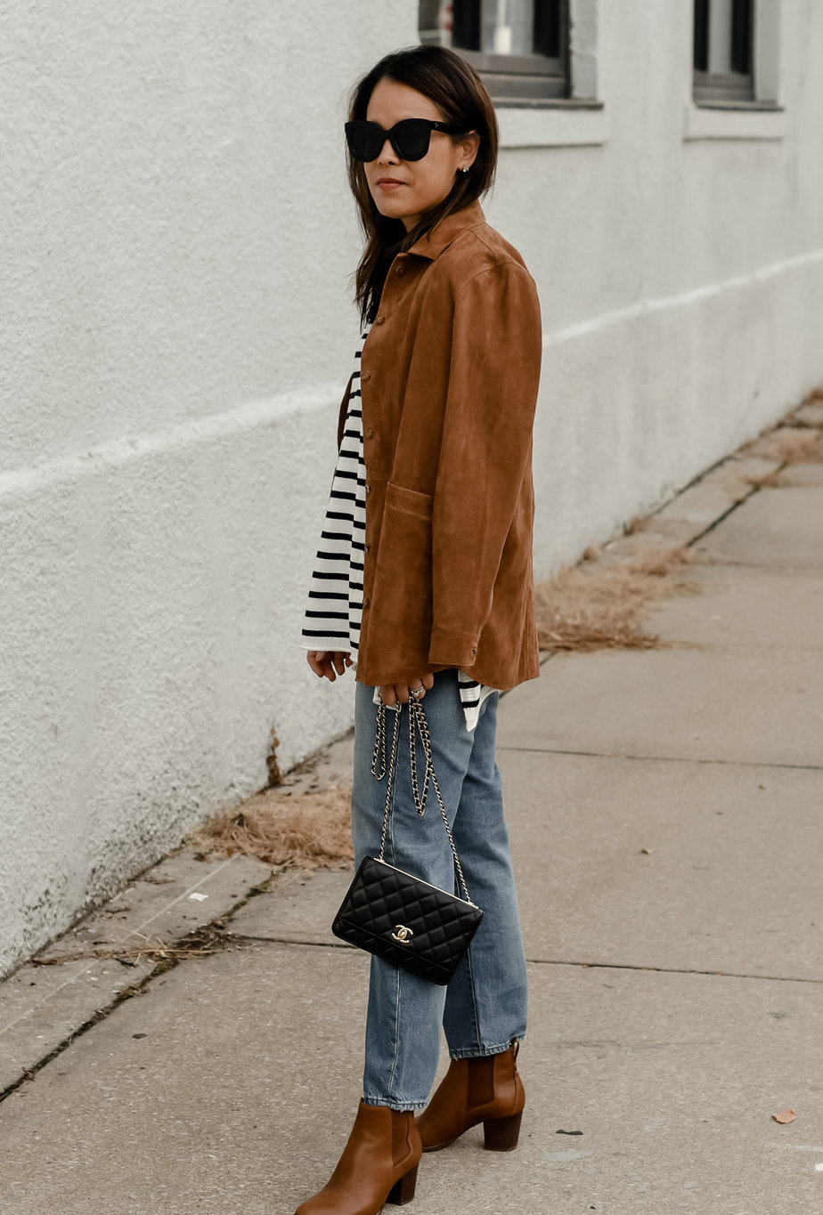 Woman showing sezane sizing wearing sezane camel jacket with stripe top and jeans.