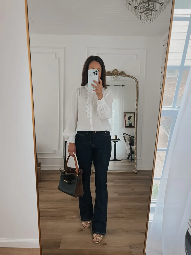 silk blouse with dark jeans Woman wearing silk blouse with dark jeans, gold sandals, and dark handbag taking picture in front of a mirror.