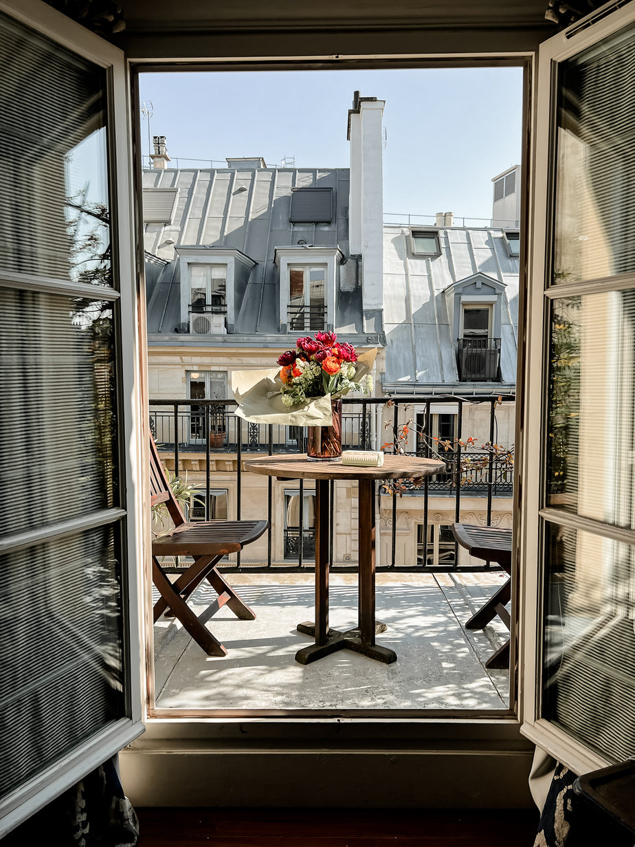 Balcony doors looking out to Paris facades with table and flowers in the middle 