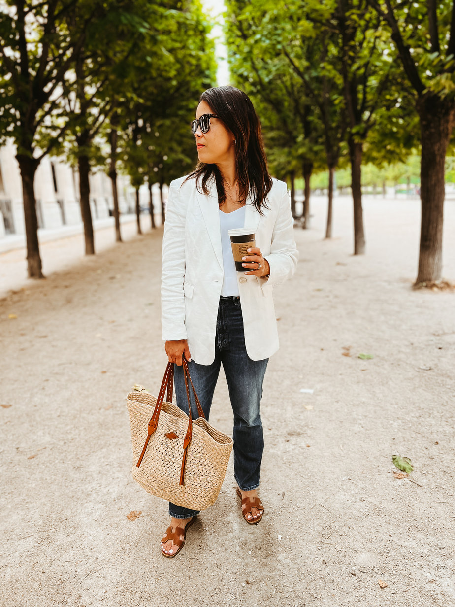 Wearing a white blazer with jeans, sandals, and Bash Paris market bag.