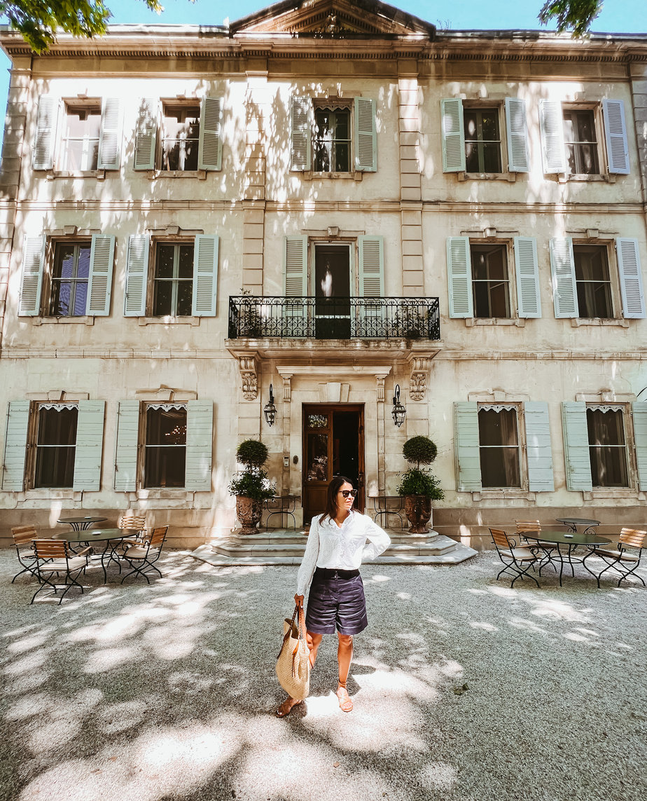white eyelet top with navy shorts and sandals standing in front of hotel in provence.