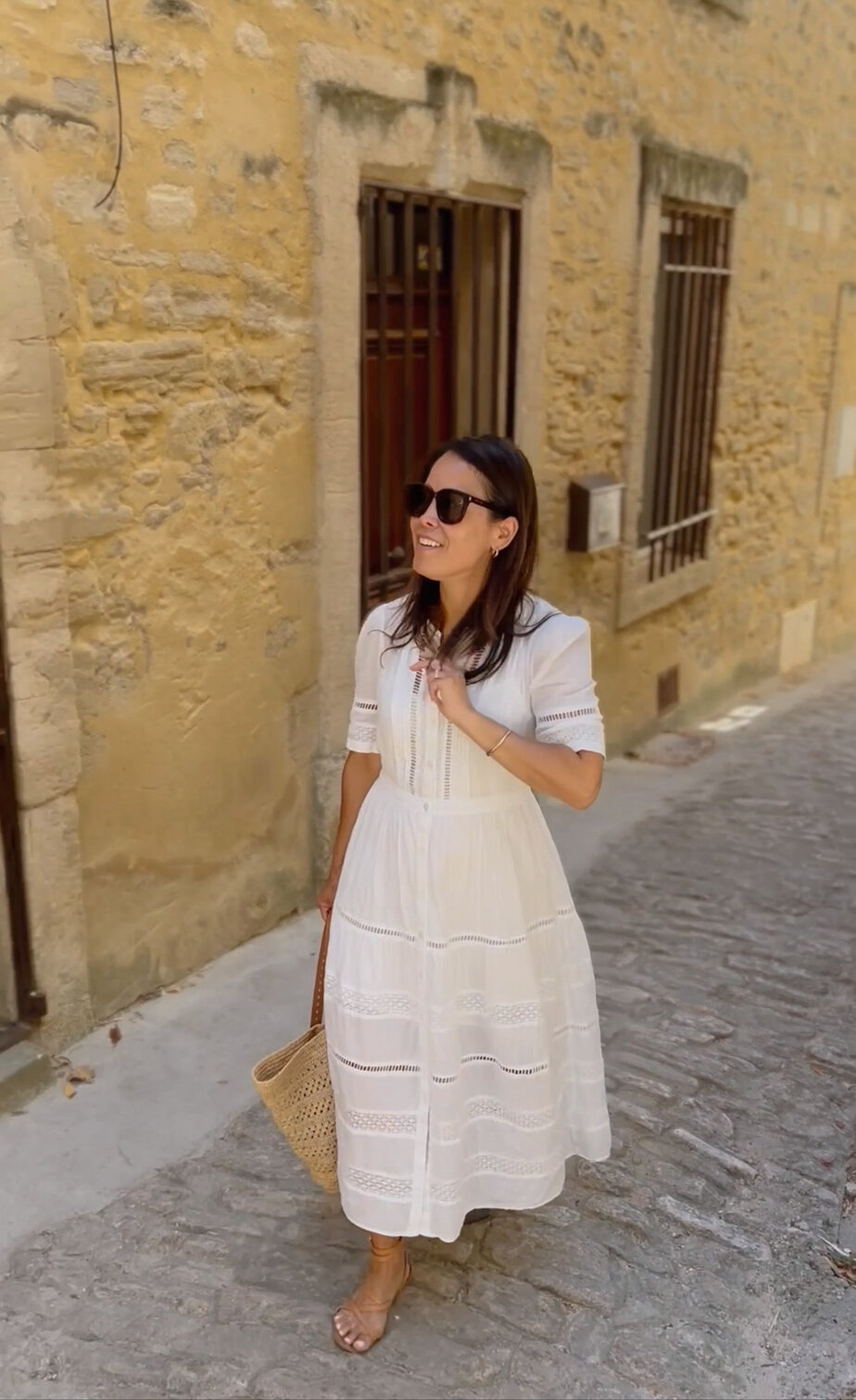 Wearing white eyelet dress with sezane sandals walking through Gordes