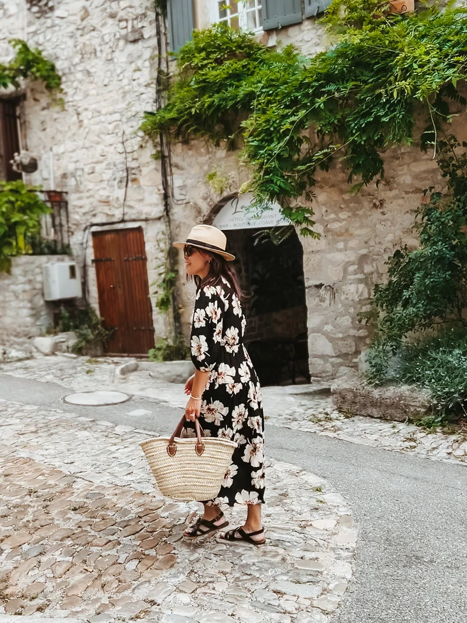 Black floral bash paris dress with sezane sandals, market tote, hat walking through village in Provence