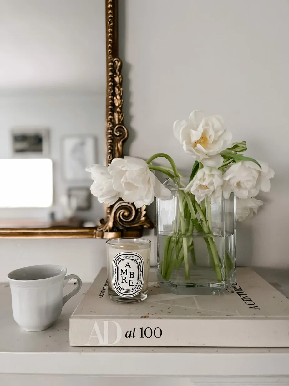 flowers in a vase on a mantle with candle and coffee cup