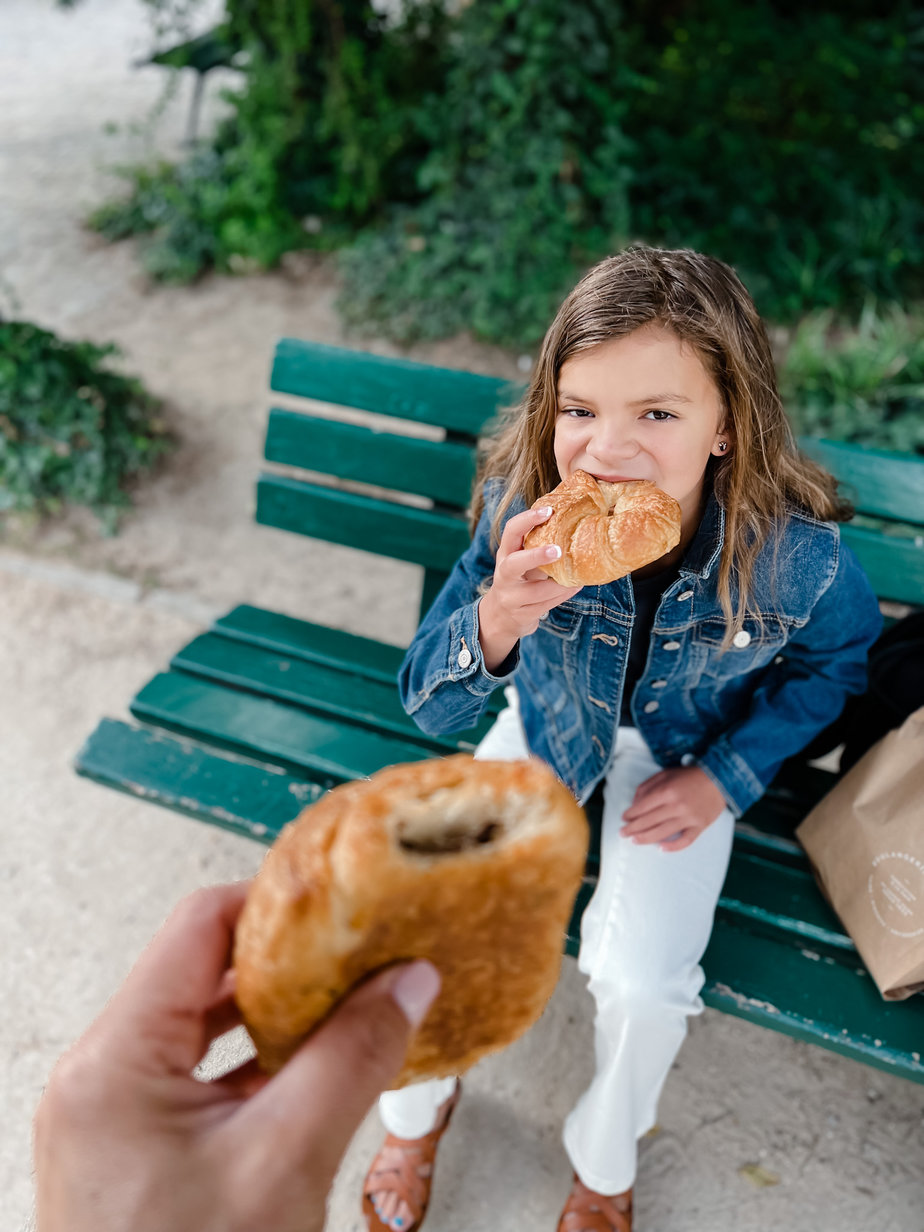 Little girl eating a chocolate croissant on a bench