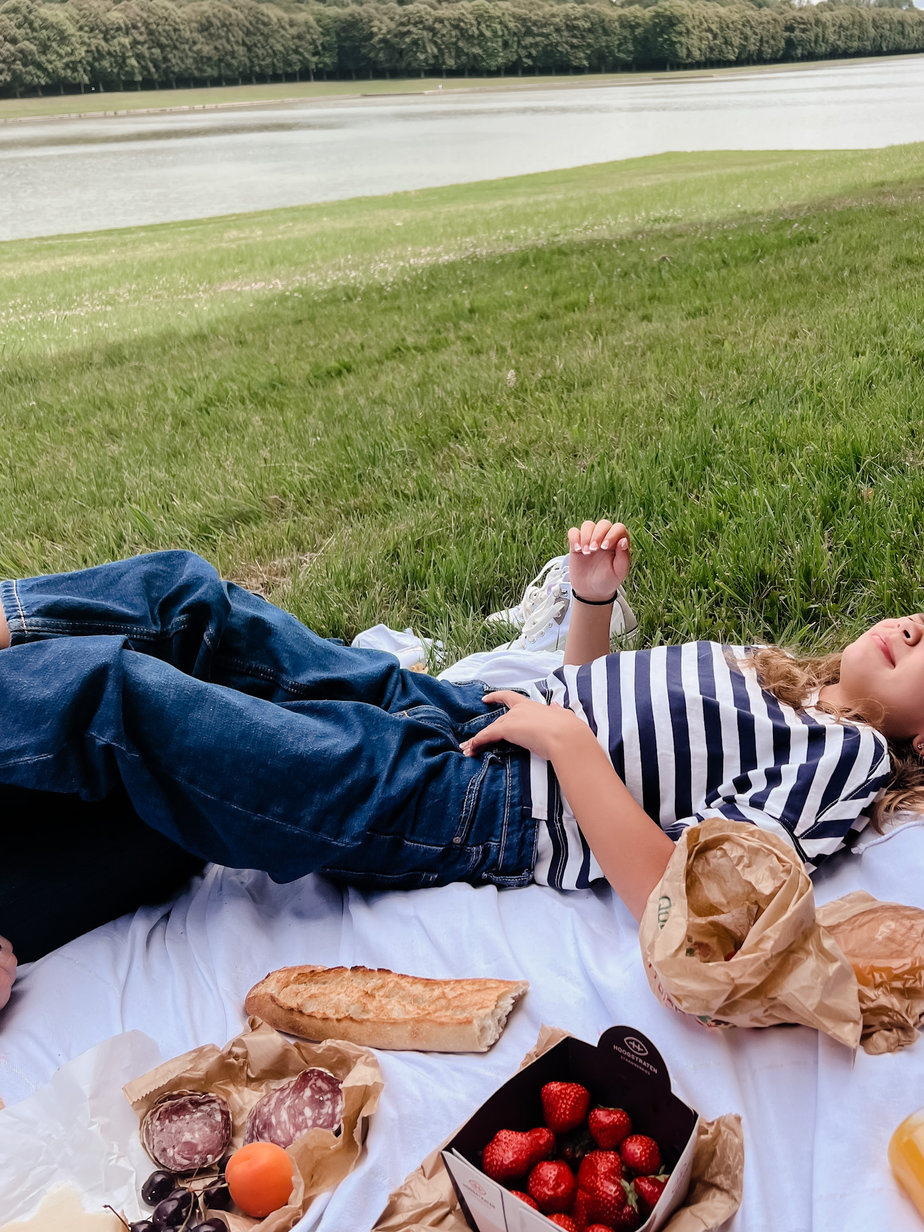 child laying on a picnic blanket with strawberries and baguette