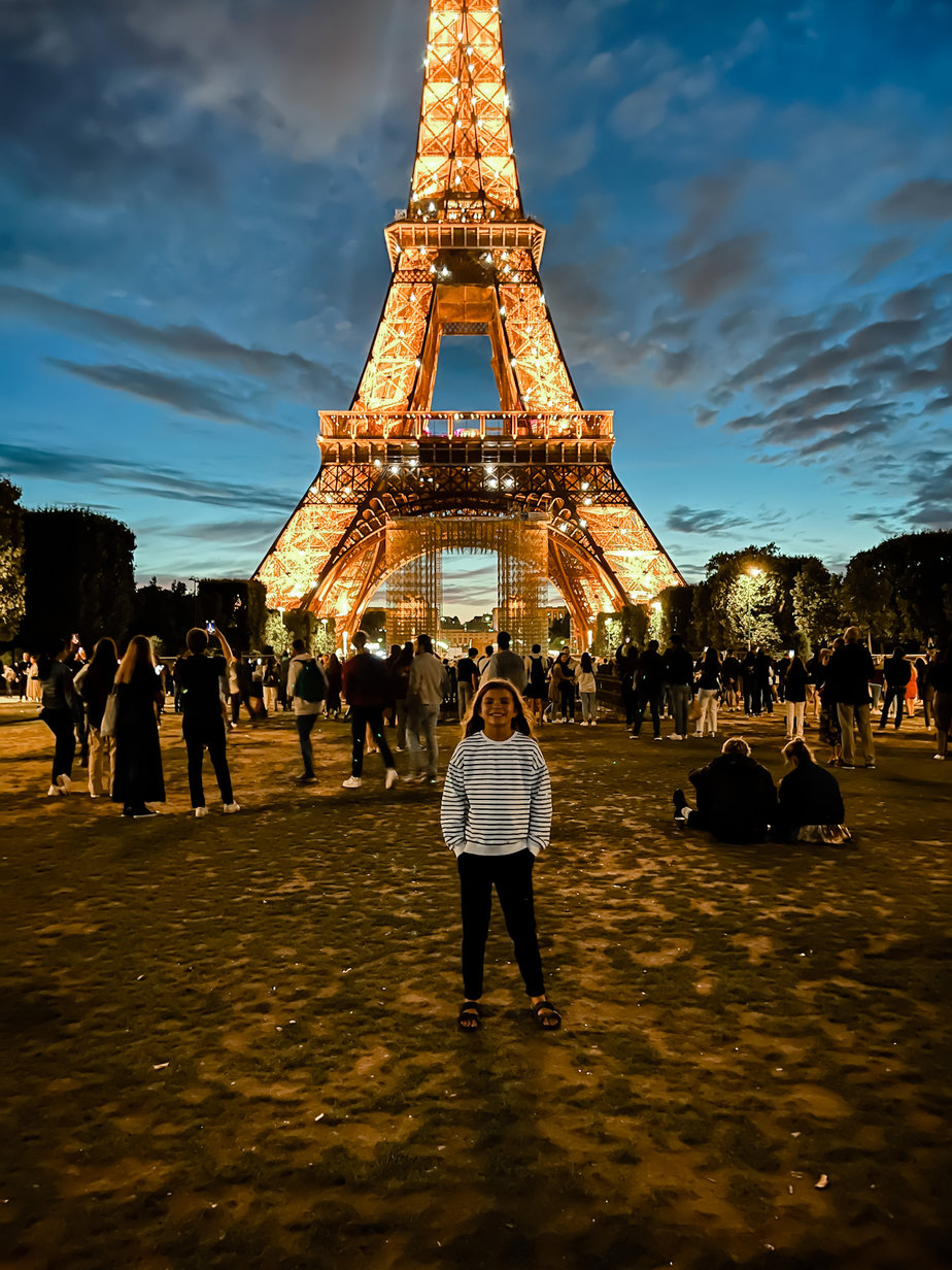 Little girl standing in front of eiffel tower while it sparkles at night 