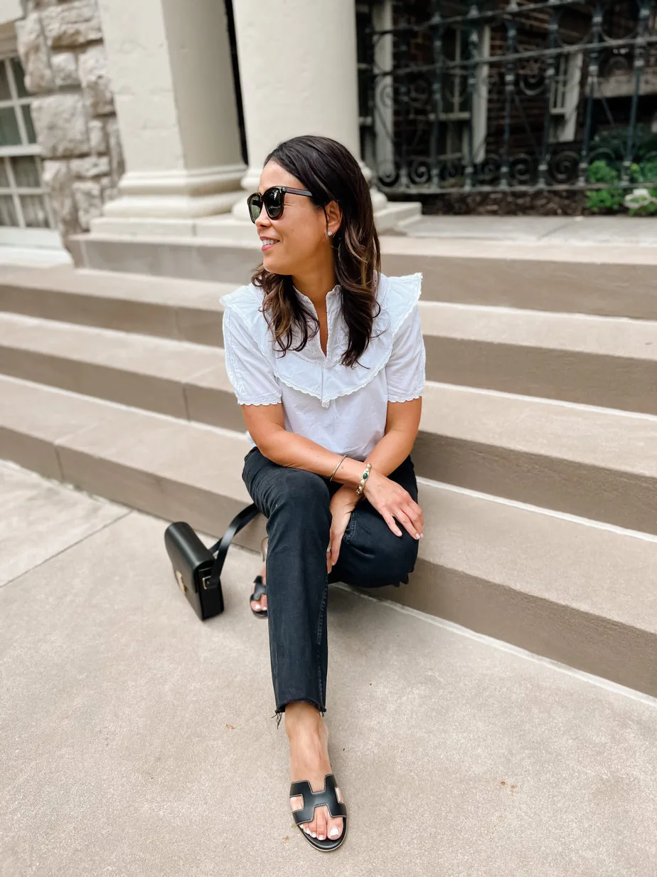 Sitting on the ground in a white top with black jeans and hermes sandals