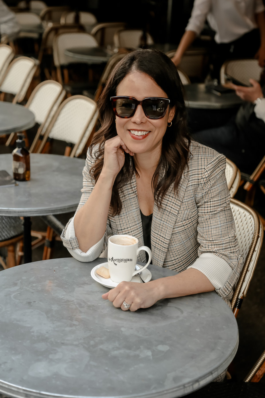 wearing a plaid blazer and sitting at a table with coffee cup in front