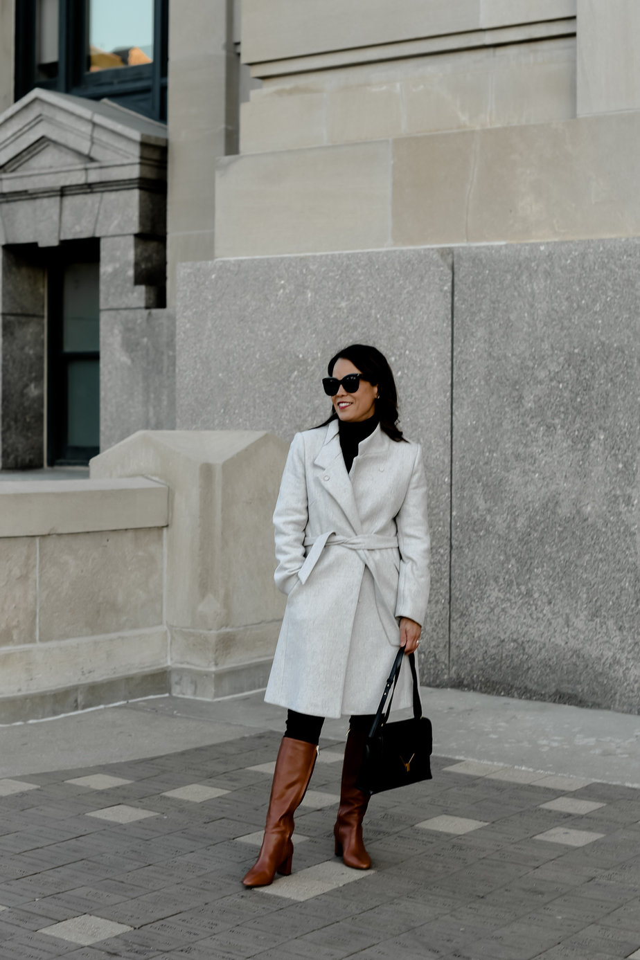 Lady with grey coat Lady with grey coat, brown tall boots, black leather bag, and black sunglasses on a cloudy cold day in front of a building