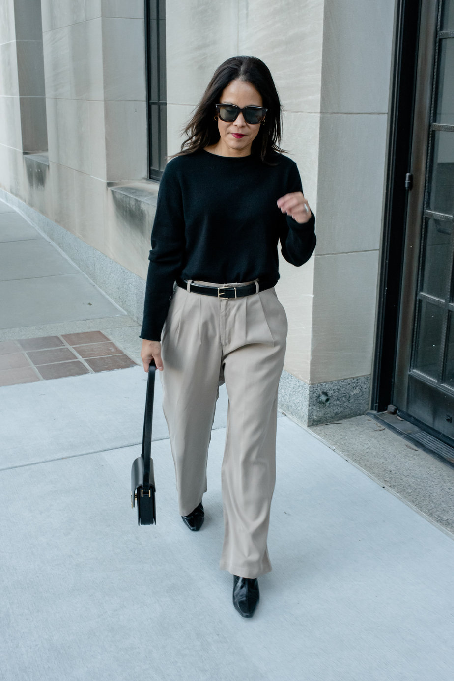 Woman wearing black sweater wearing trousers, black belt, black boots, and black leather handbag