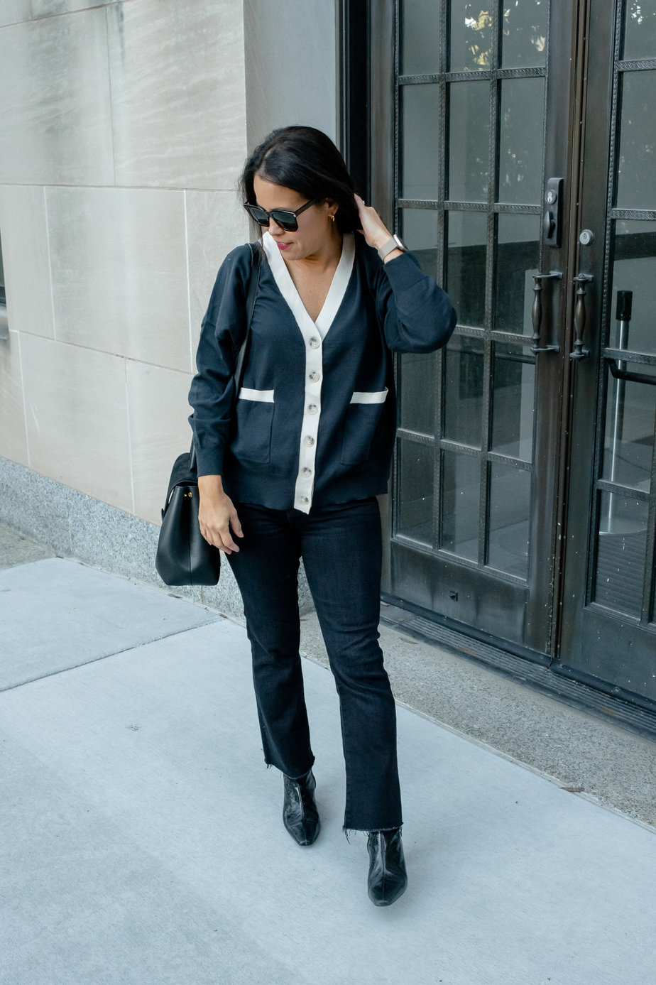 black jeans, boots, and black handbag standing against a wall