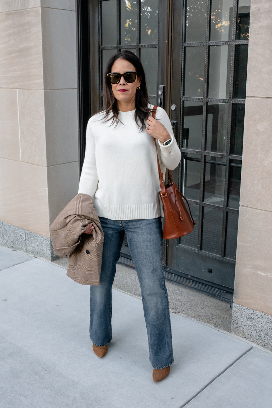 Woman in a cream cashmere sweater standing against a black door