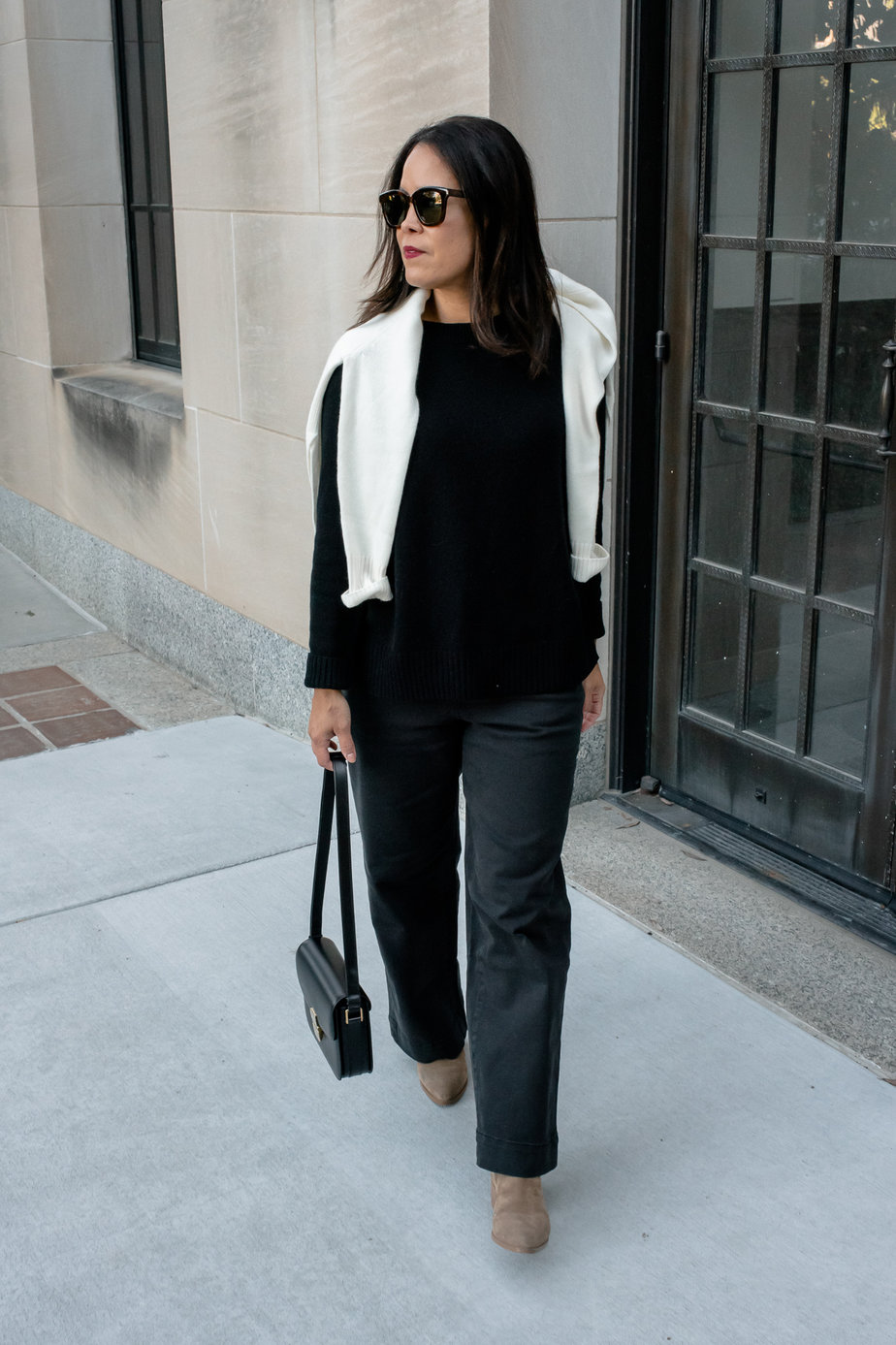 Black Mer Sea cashmere sweater with black pants, cream sweater draped over shoulders of a woman walking