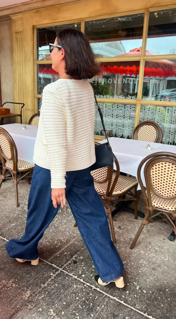 cream cardigan with jeans Woman walking wearing cream cardigan with jeans and pumps walking in front of a restaurant.