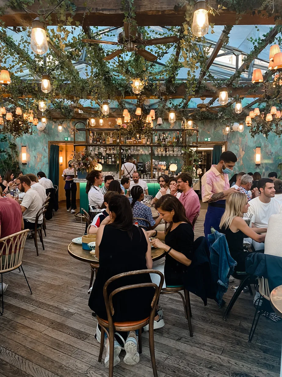 People sitting on top floor of a restaurant with greenery on celining