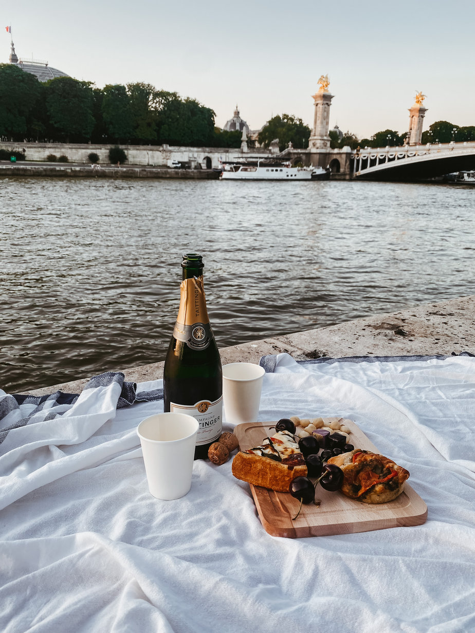 A picnic with white blanket, champagne, fruit, and paper cup