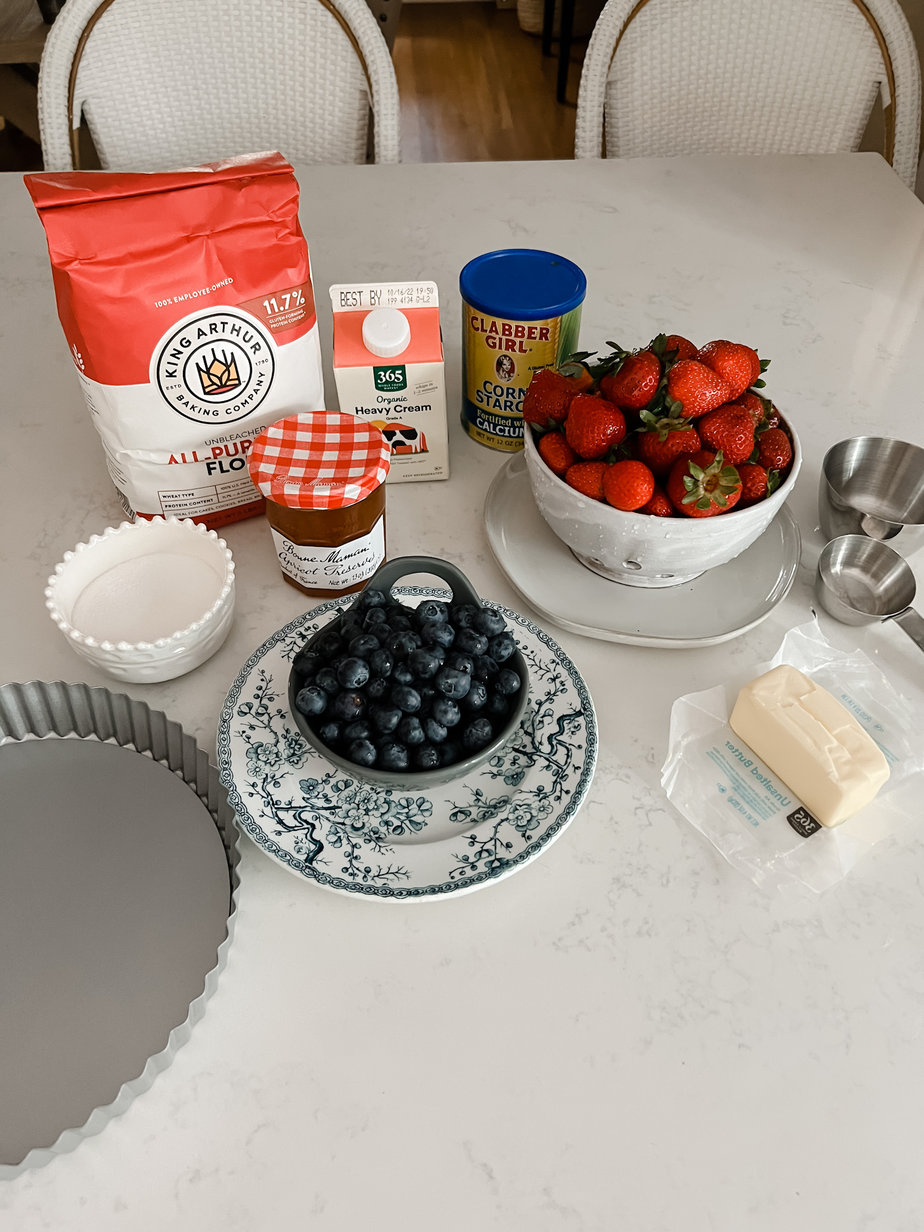 strawberries in a white bowl, blueberries on a plate, bon mamn jam, butter, kings flour sitting on a marble countertop