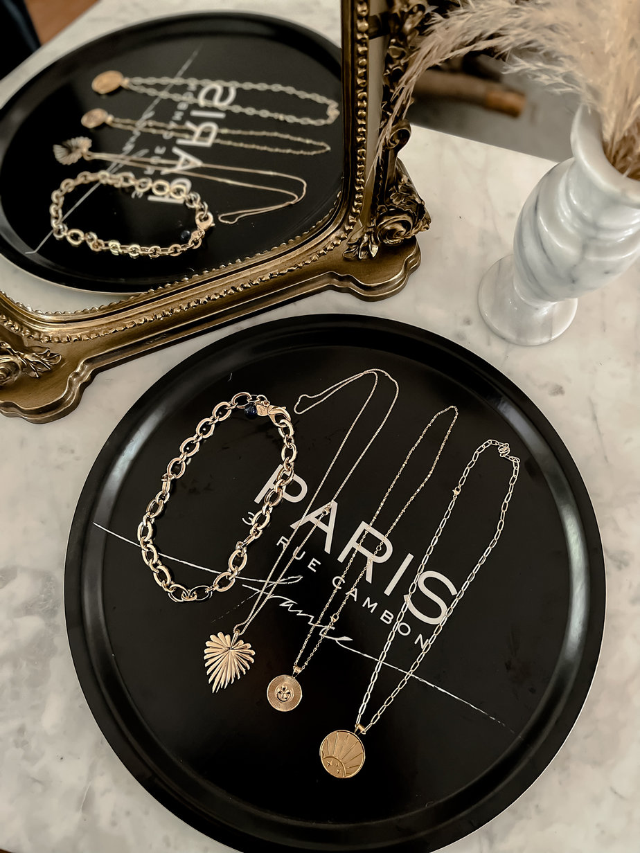 4 gold layering necklaces sitting on a black tray that says Paris